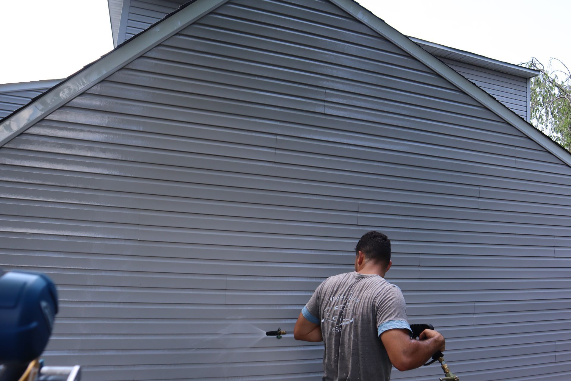 A man is cleaning the side of a house with a pressure washer