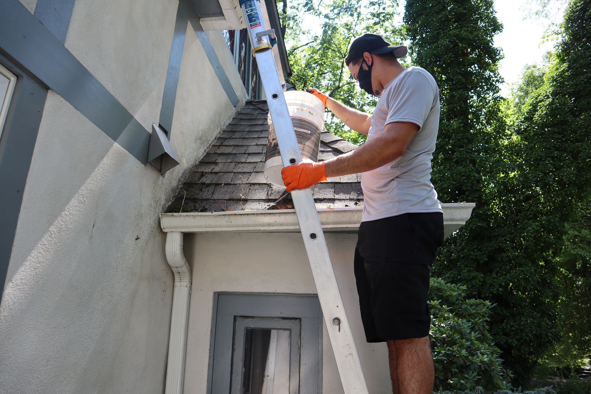 A man is standing on a ladder cleaning the gutters of a house