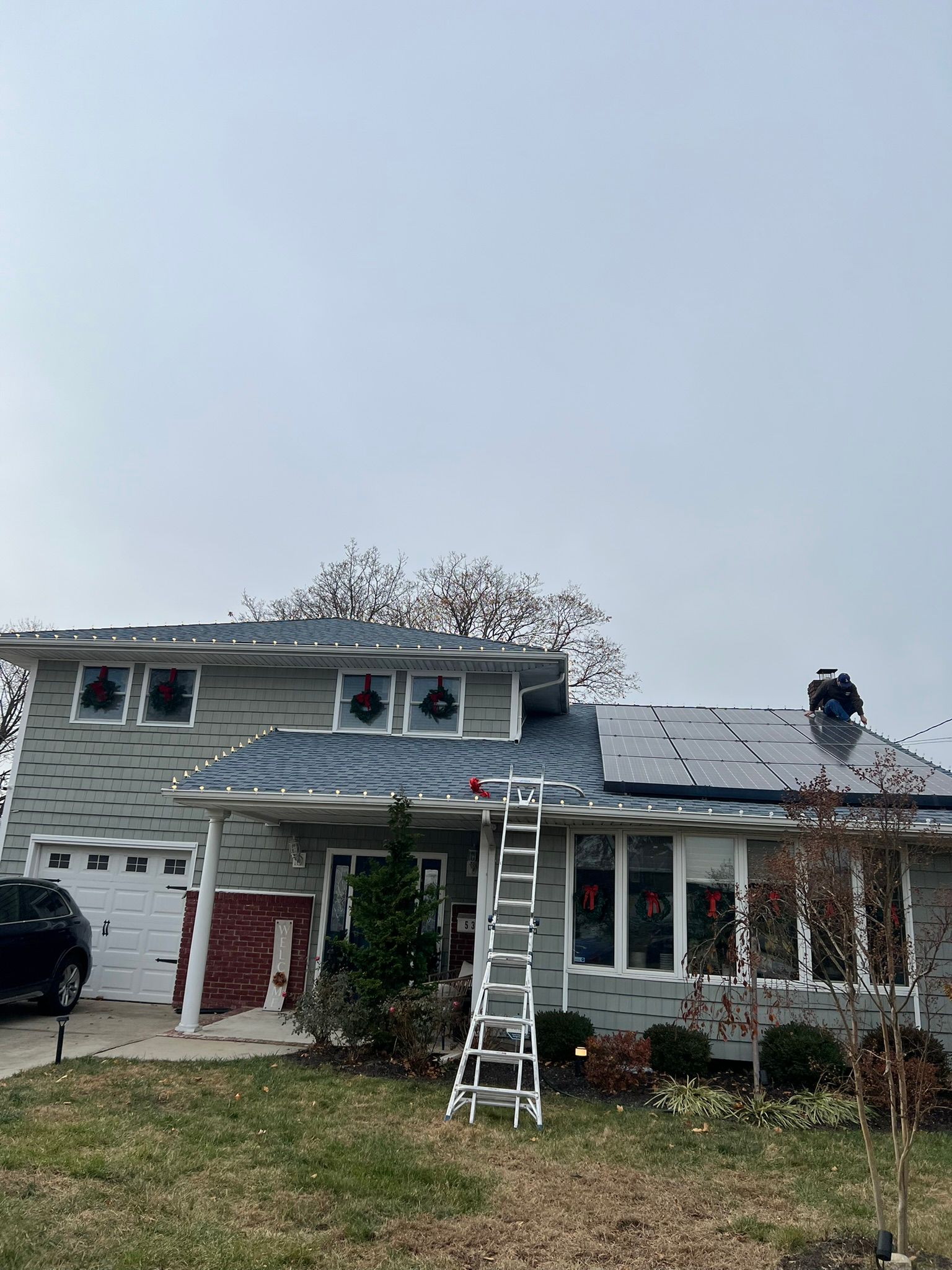 A house with a ladder in front of it is decorated with holiday lights