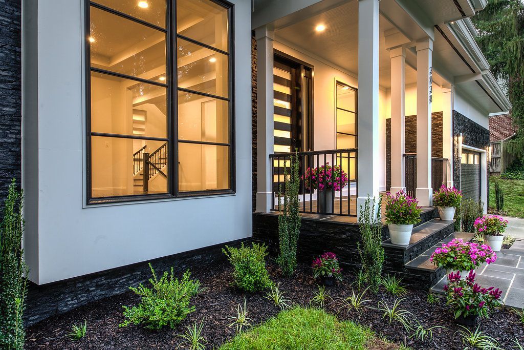 Modern house exterior with white columns, black trim, and landscaped flower beds.