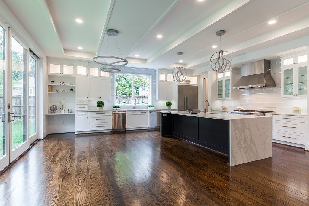 Spacious modern kitchen with white cabinetry, dark island, stainless steel appliances, and dark wood floors.