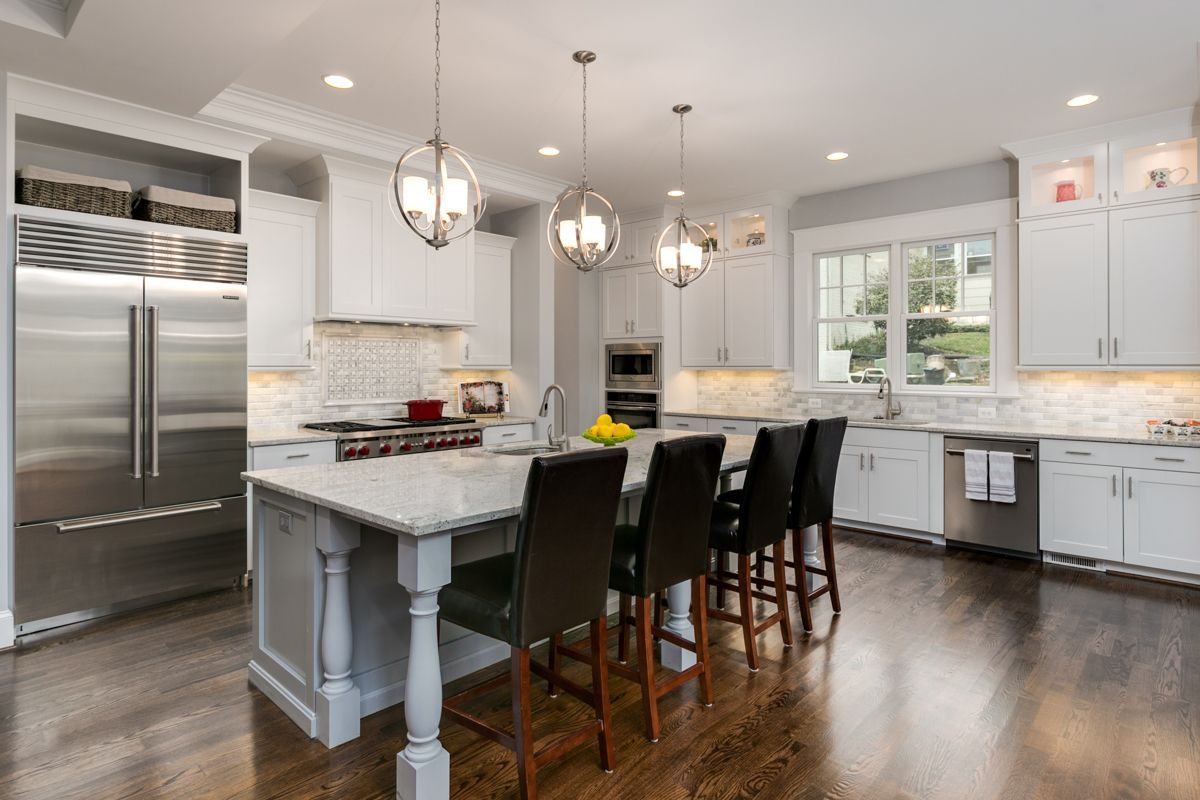 Elegant white kitchen with island, stainless steel appliances, dark wood floors, and pendant lighting.