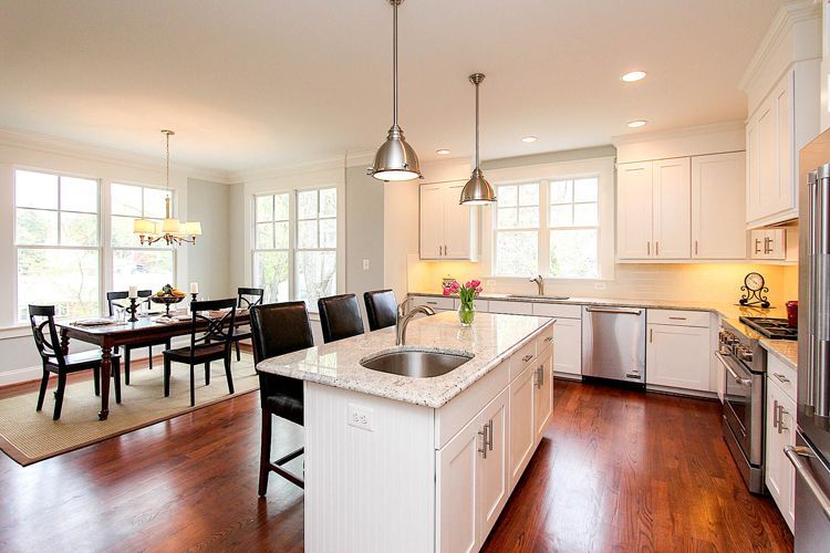 Bright kitchen with white cabinets, island with sink, dining table, dark wood floors.