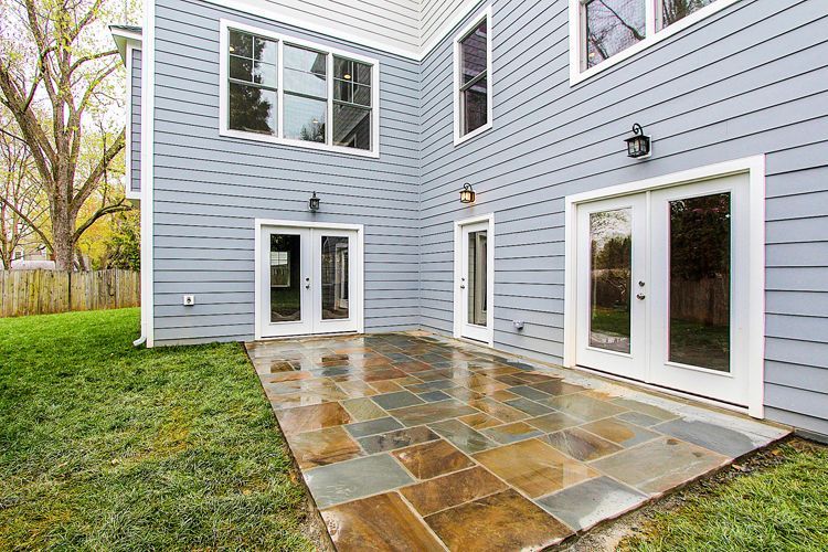 Backyard patio with stone tiles, two French doors, blue siding.