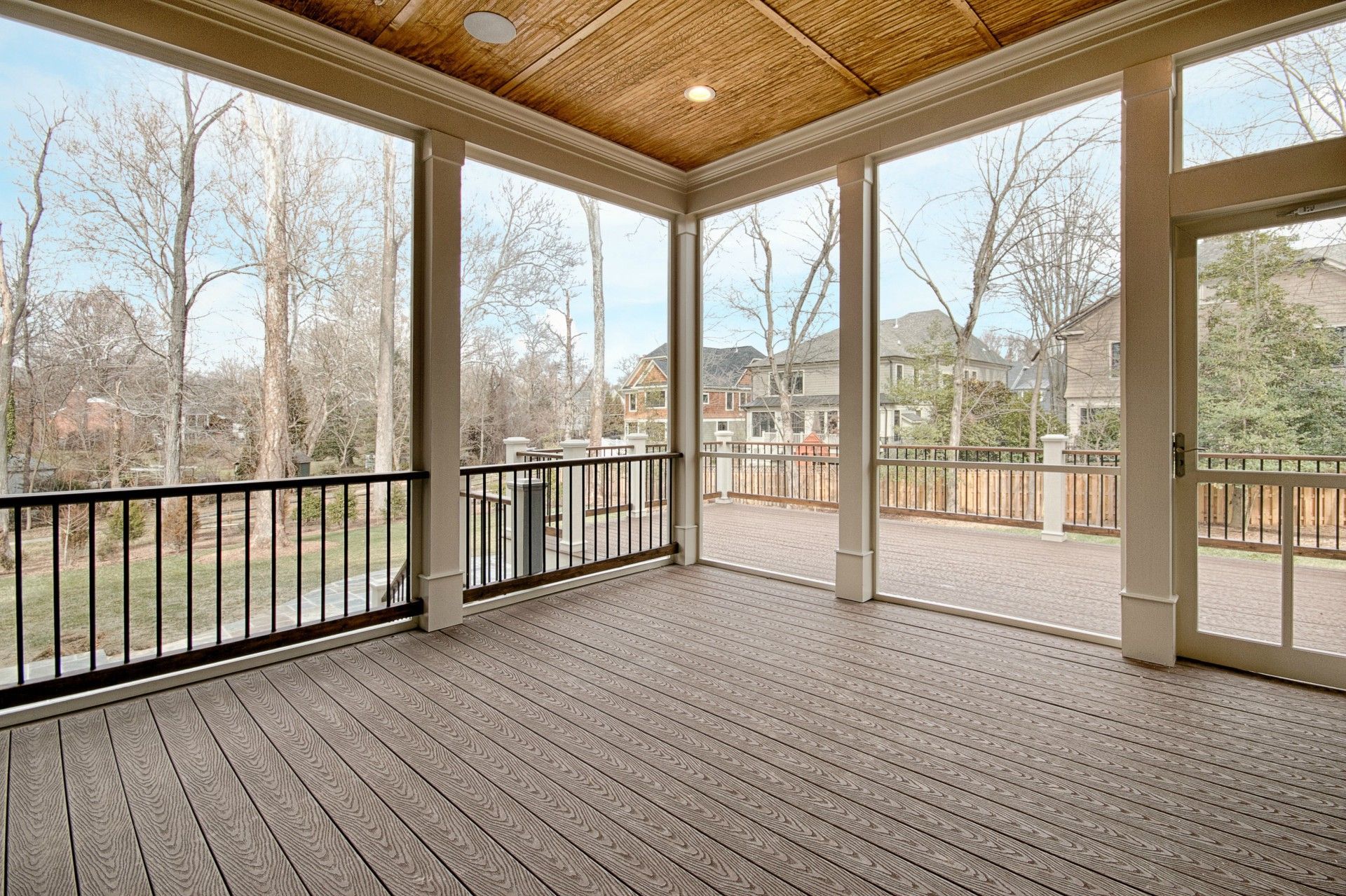Spacious screened porch with composite deck, black railing, and views of trees and houses.