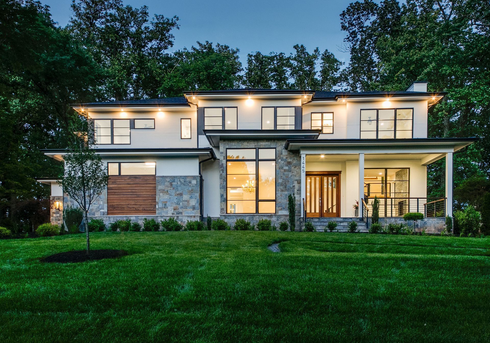 Two-story house with illuminated windows and a wooden exterior at dusk.