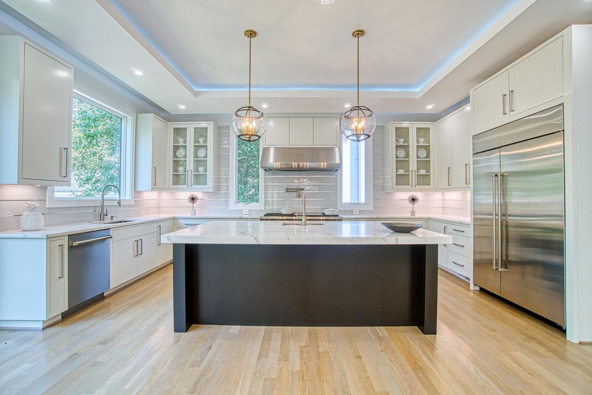 Bright white kitchen with island, marble countertops, and a view into the living room with a fireplace.