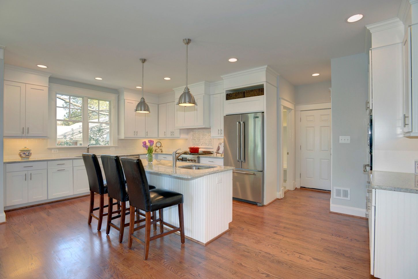 Bright white kitchen with island, stainless steel refrigerator, and hardwood floors.