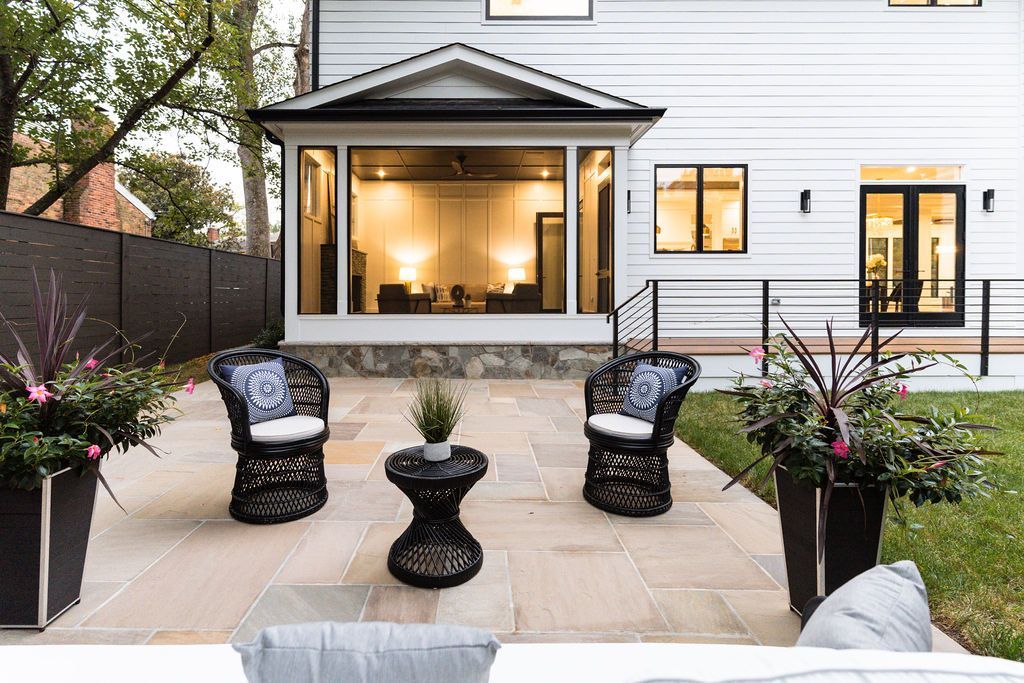Patio with wicker chairs and a small table, next to a house with large windows.