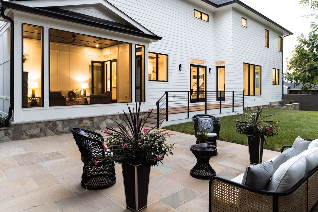 Backyard patio with wicker furniture, large windows, and white house.