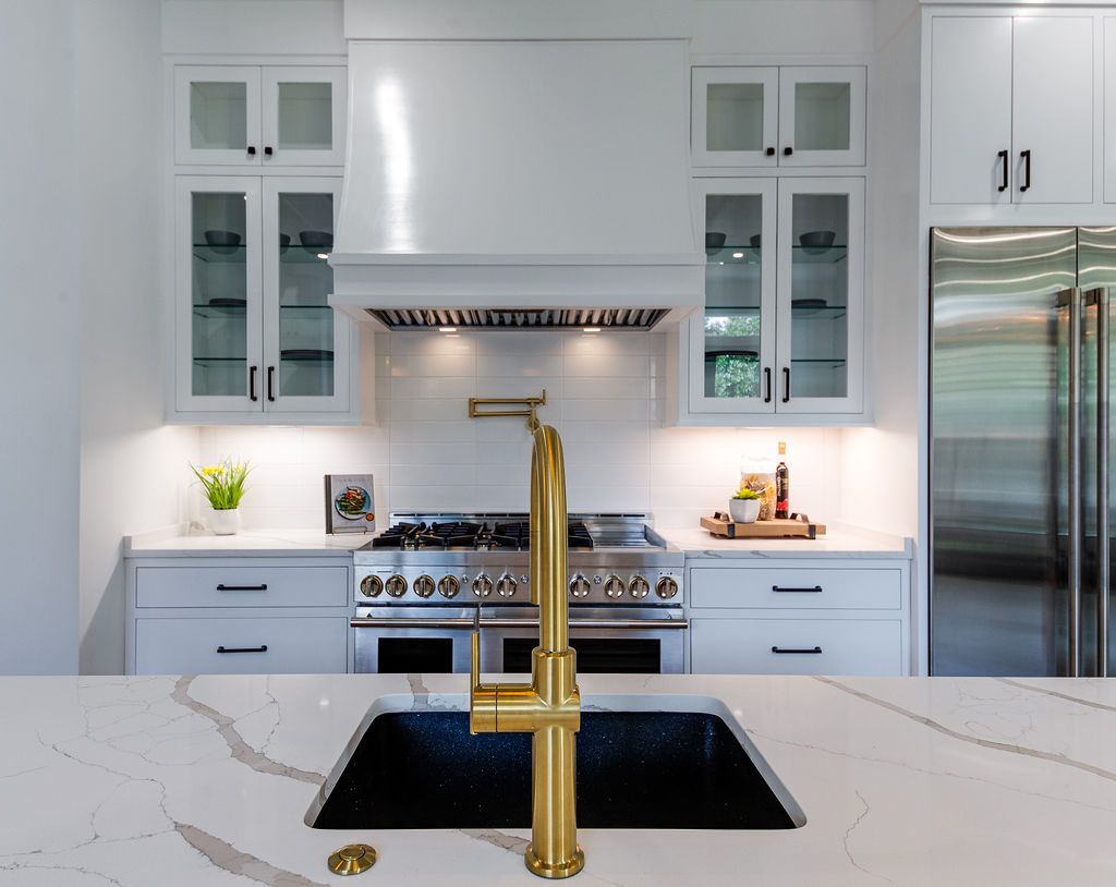 Gold faucet over a black kitchen sink in a modern white kitchen with stainless steel appliances.