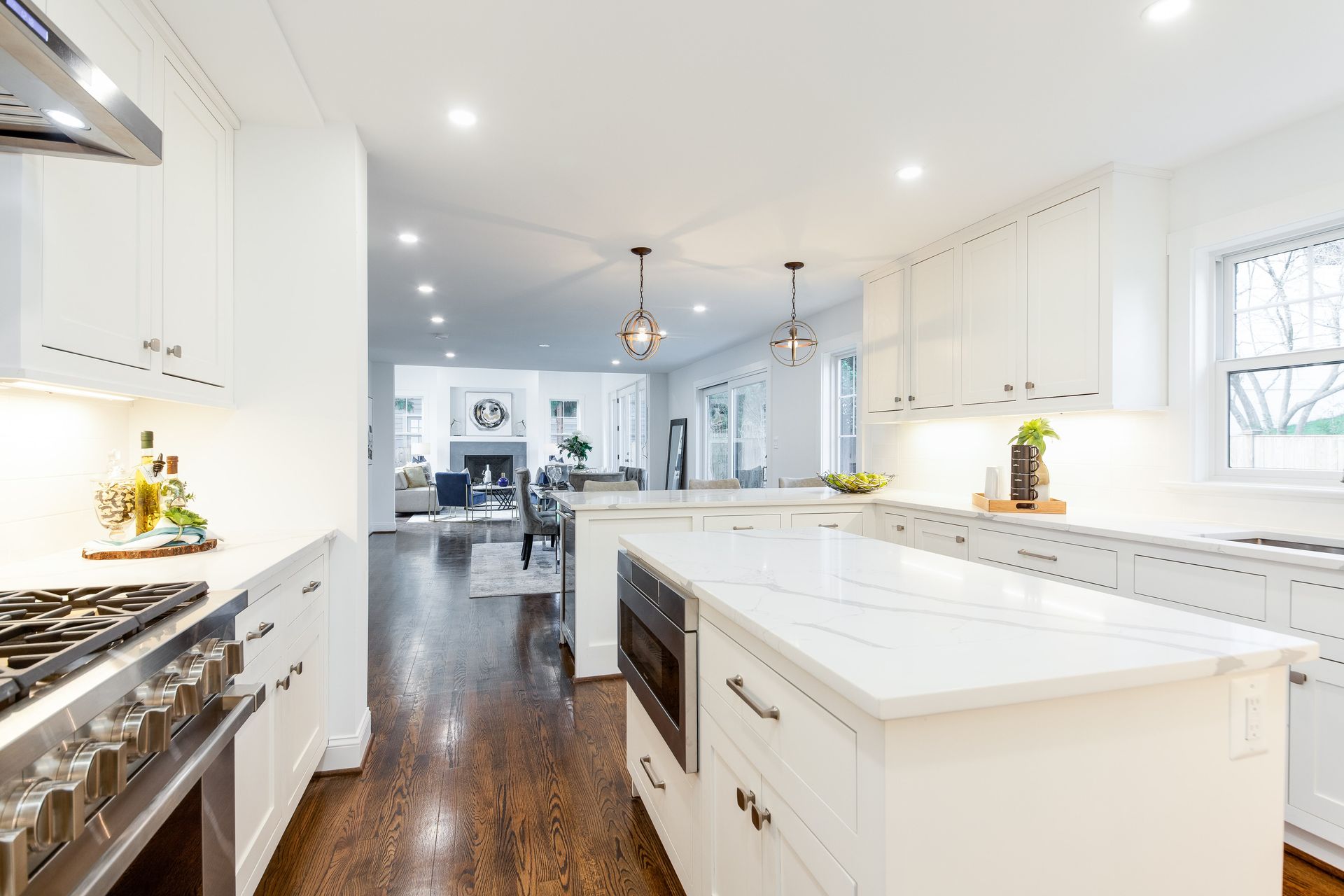 Bright white kitchen with island, marble countertops, and a view into the living room with a fireplace.