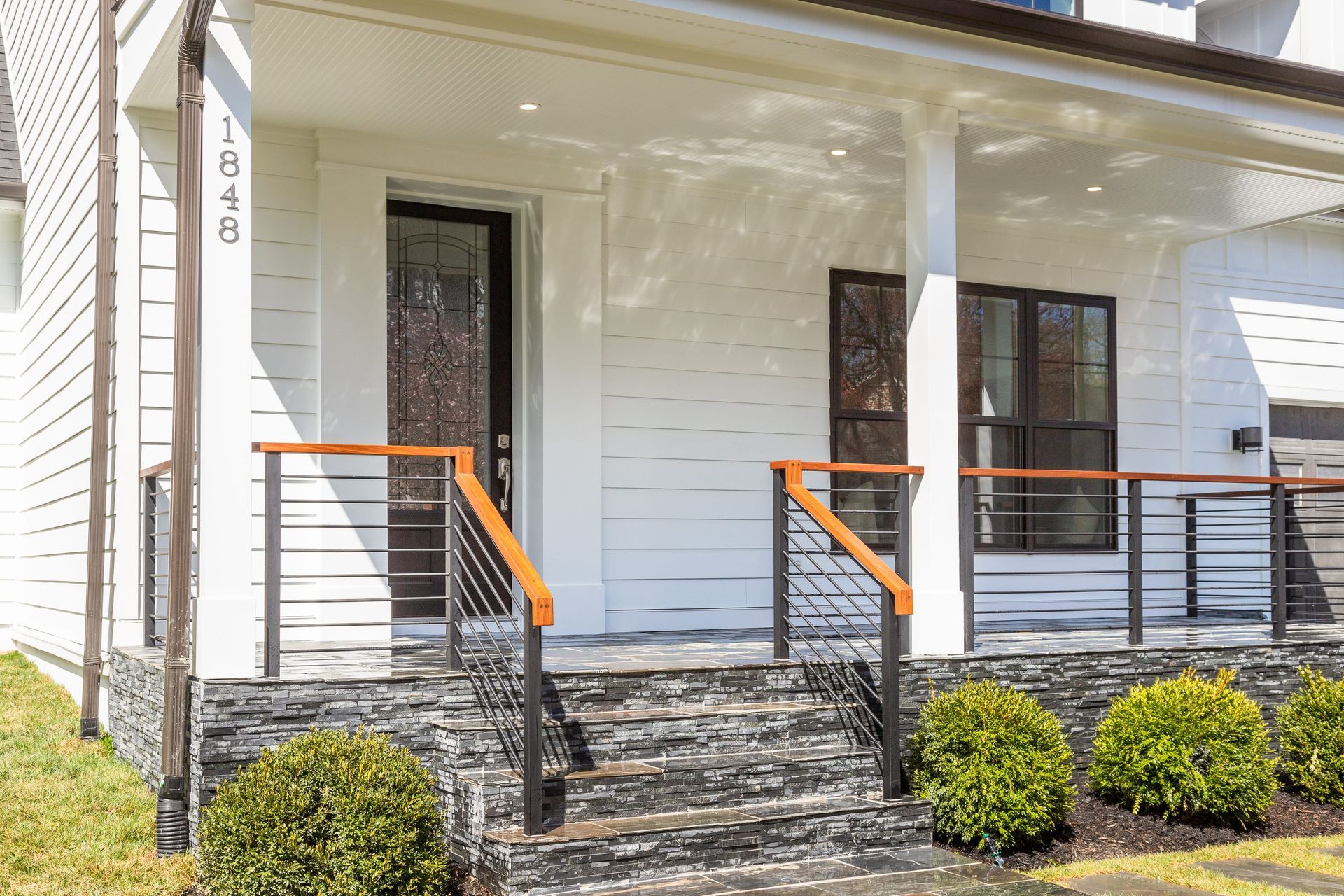 White house with front porch, steps, black and wood railings, and front door.