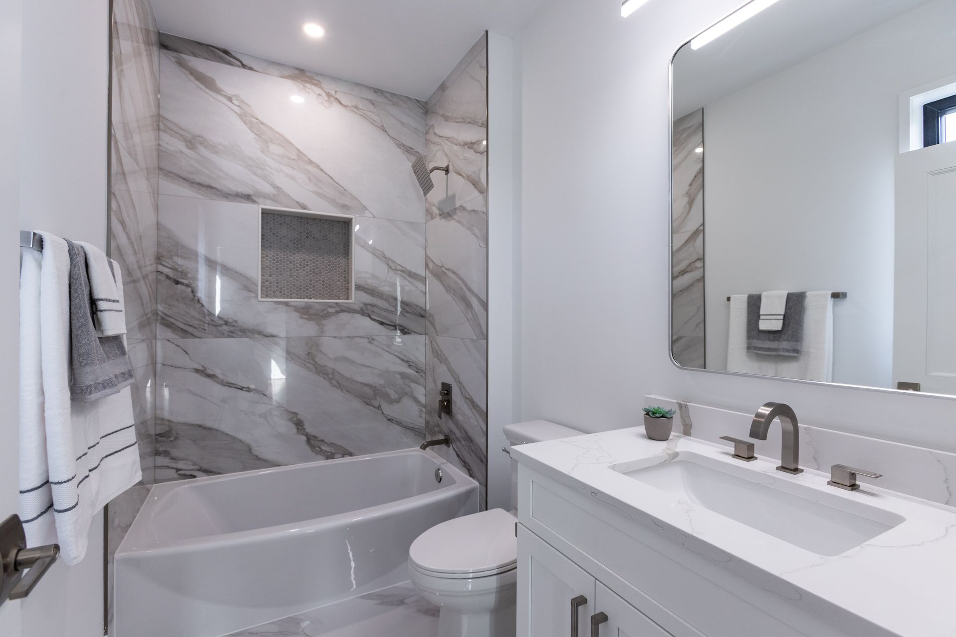 White bathroom with marble shower, vanity, toilet, and towel rack.