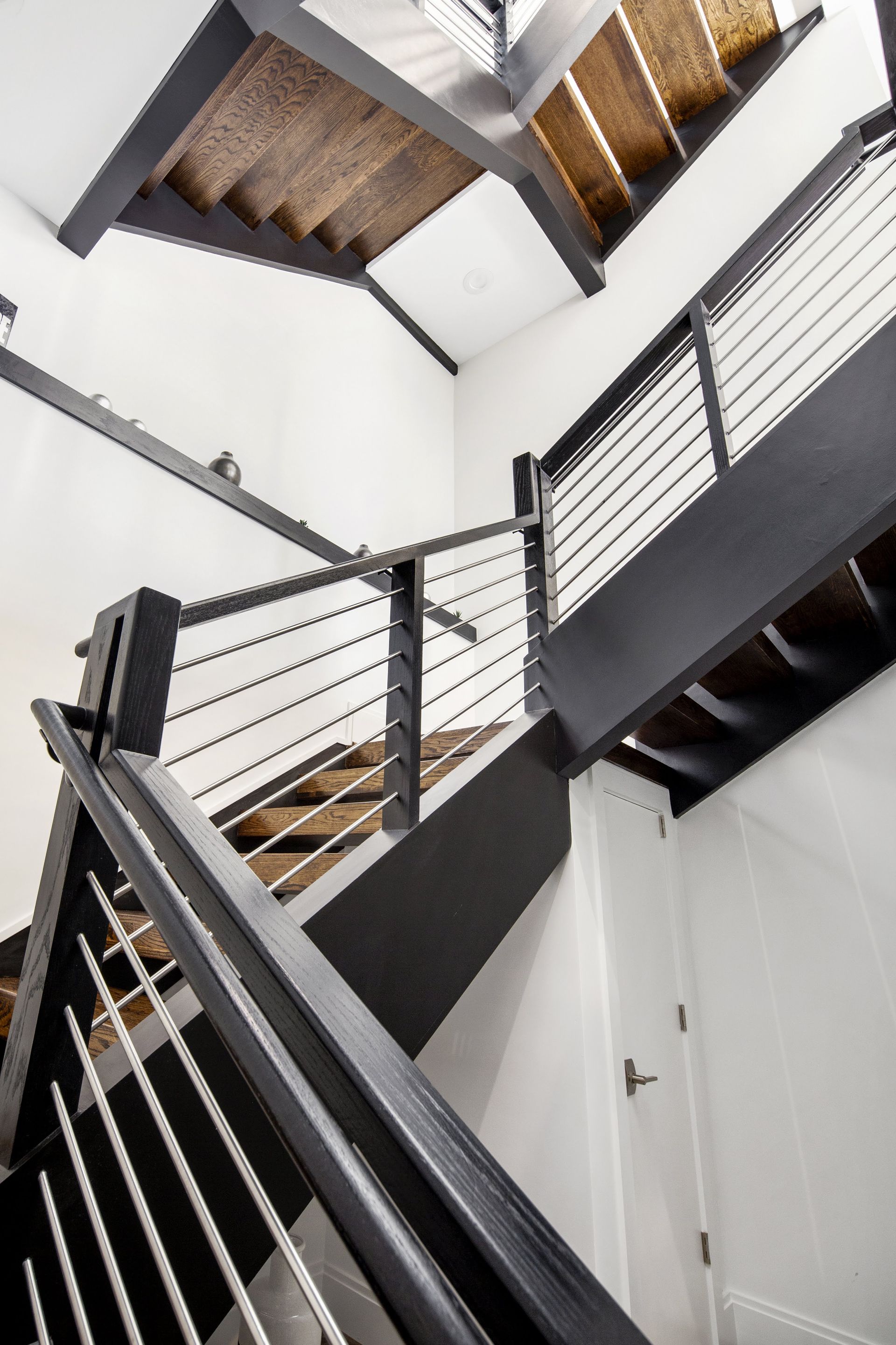 Modern staircase with black steel frame, cable railings, wooden treads. White walls.