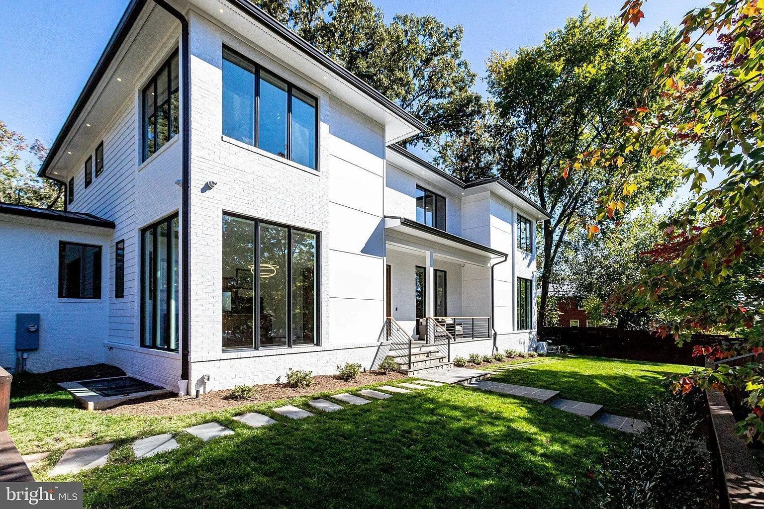 Modern white house with dark framed windows, lawn, and stepping stones.
