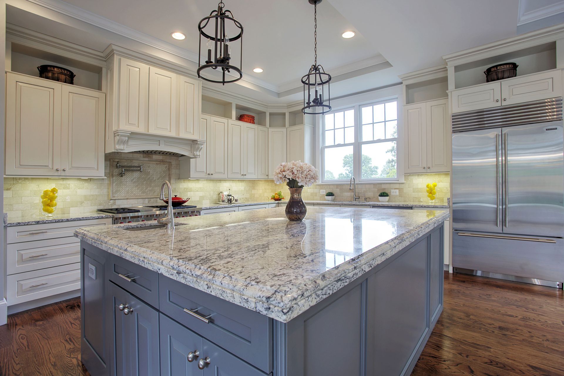 Elegant kitchen with gray island, white cabinets, granite countertops, and stainless steel appliances.