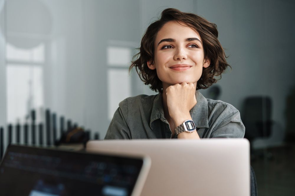 A woman is sitting in front of a laptop computer and smiling.