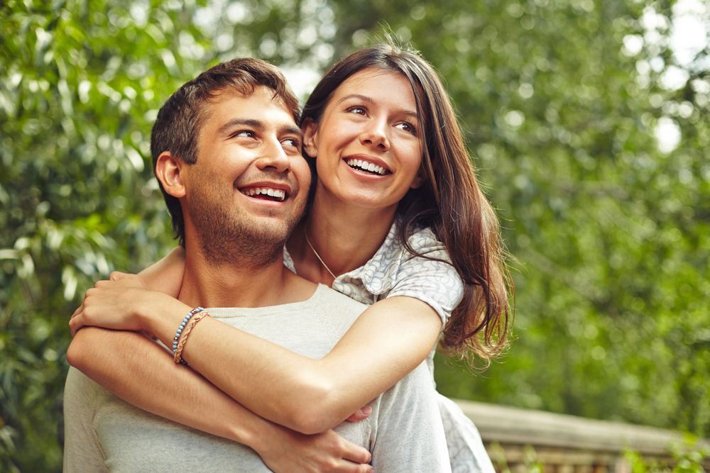 A man is carrying a woman on his back in a park.