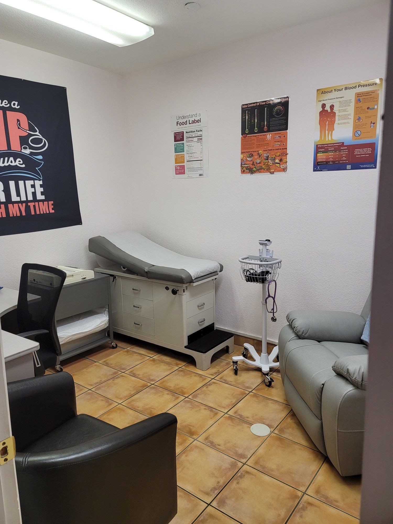 A doctor 's office with a couch , chair , desk and examination table.