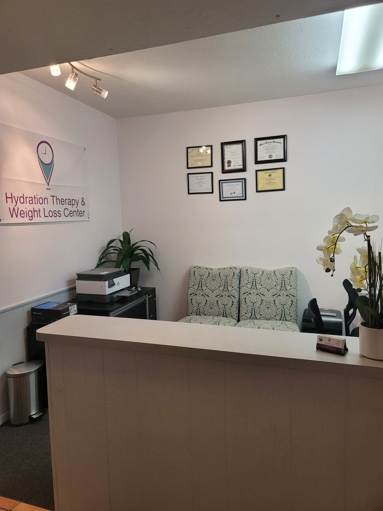 A waiting room with a couch and a desk with a lot of certificates on the wall.