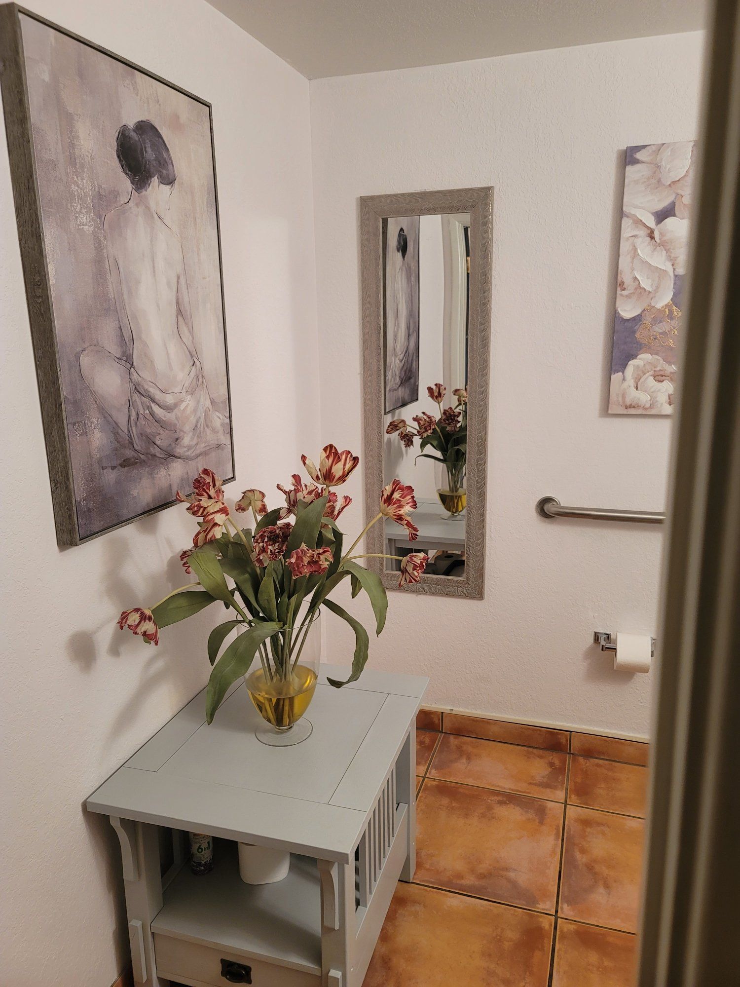A bathroom with a vase of flowers on a table and a mirror.