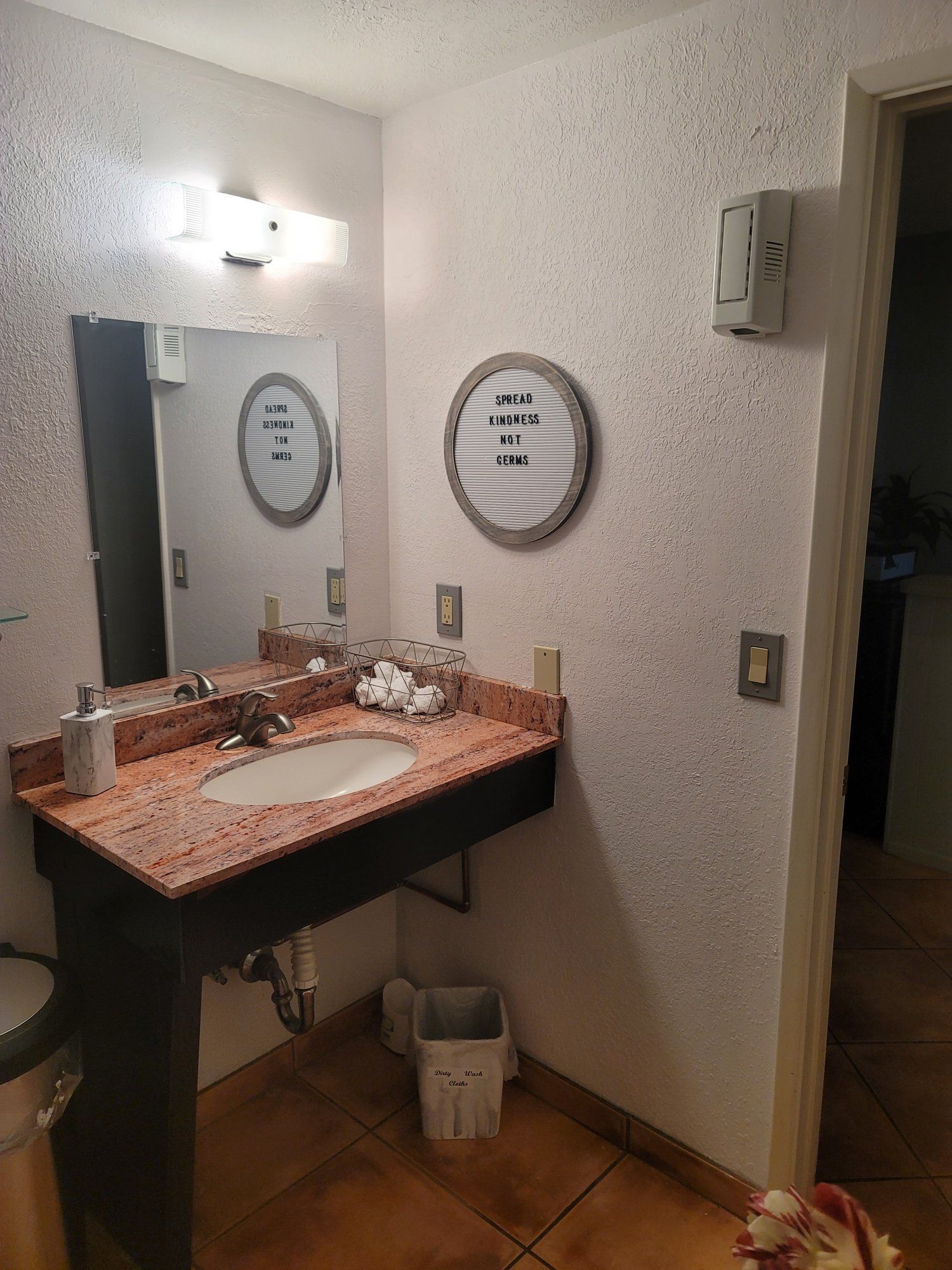 A bathroom with a sink , mirror and trash can.