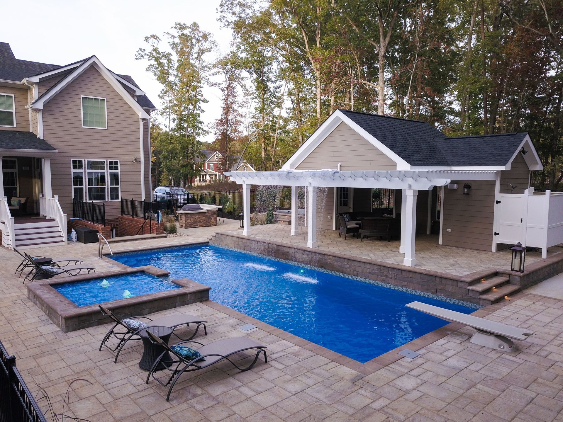 Backyard with pool, hot tub, lounge chairs, pergola, cabana, and large house.
