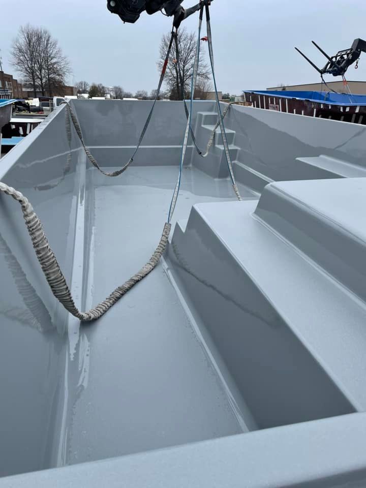 Empty, gray rectangular pool shell being lifted by a crane outdoors. Steps and a bench are visible.