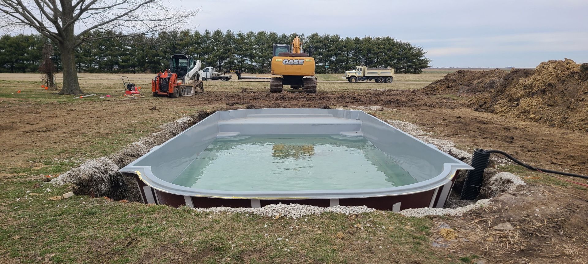 Pool being installed with heavy machinery in a rural outdoor setting.