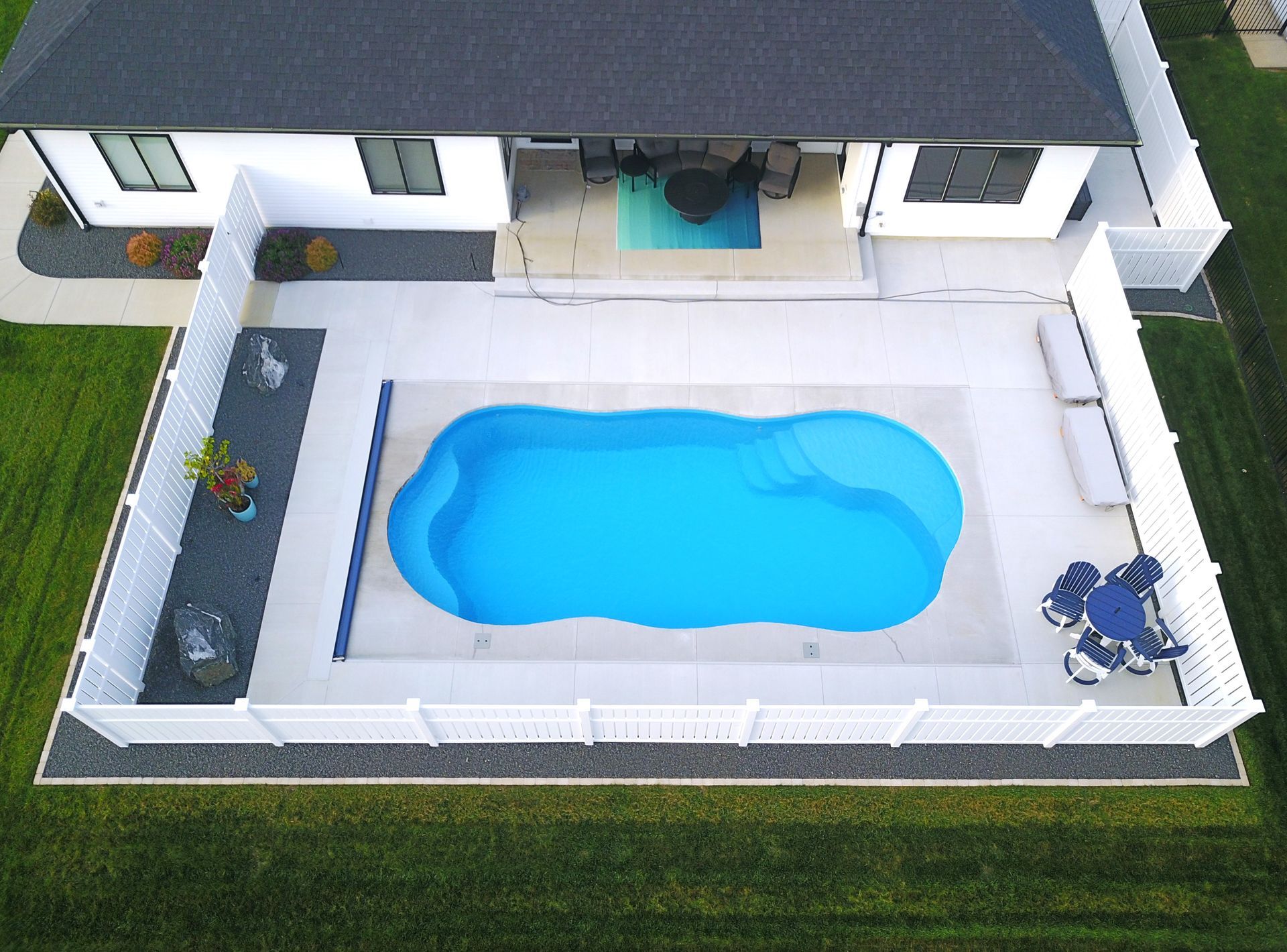 Aerial view of a swimming pool surrounded by a white fence and a house with a black roof.
