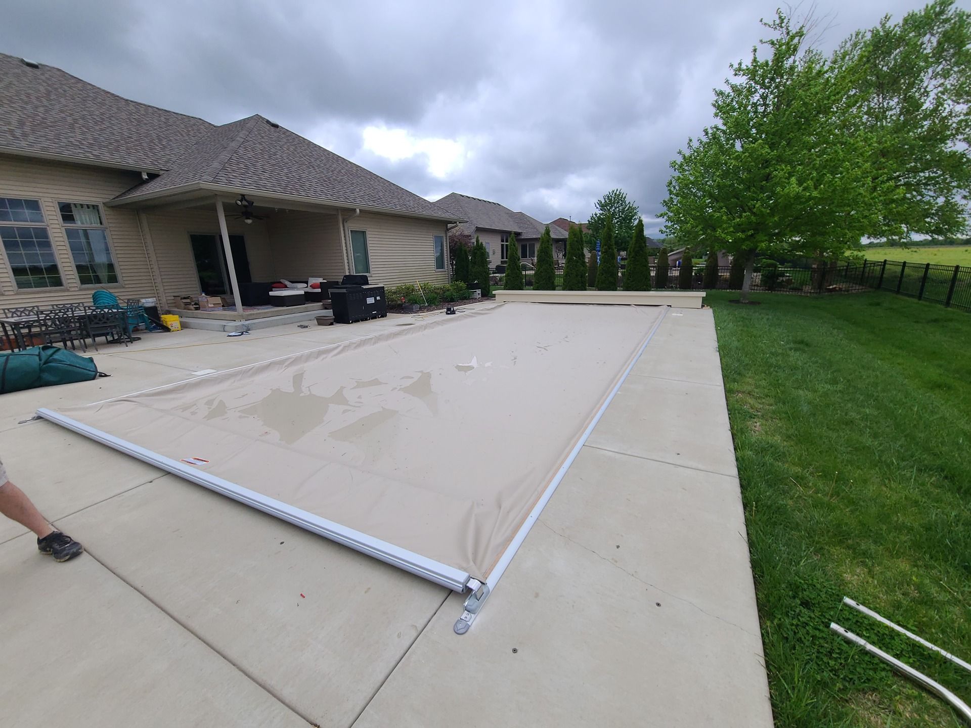 A pool cover laid out on a concrete patio. A house is in the background. Overcast sky.
