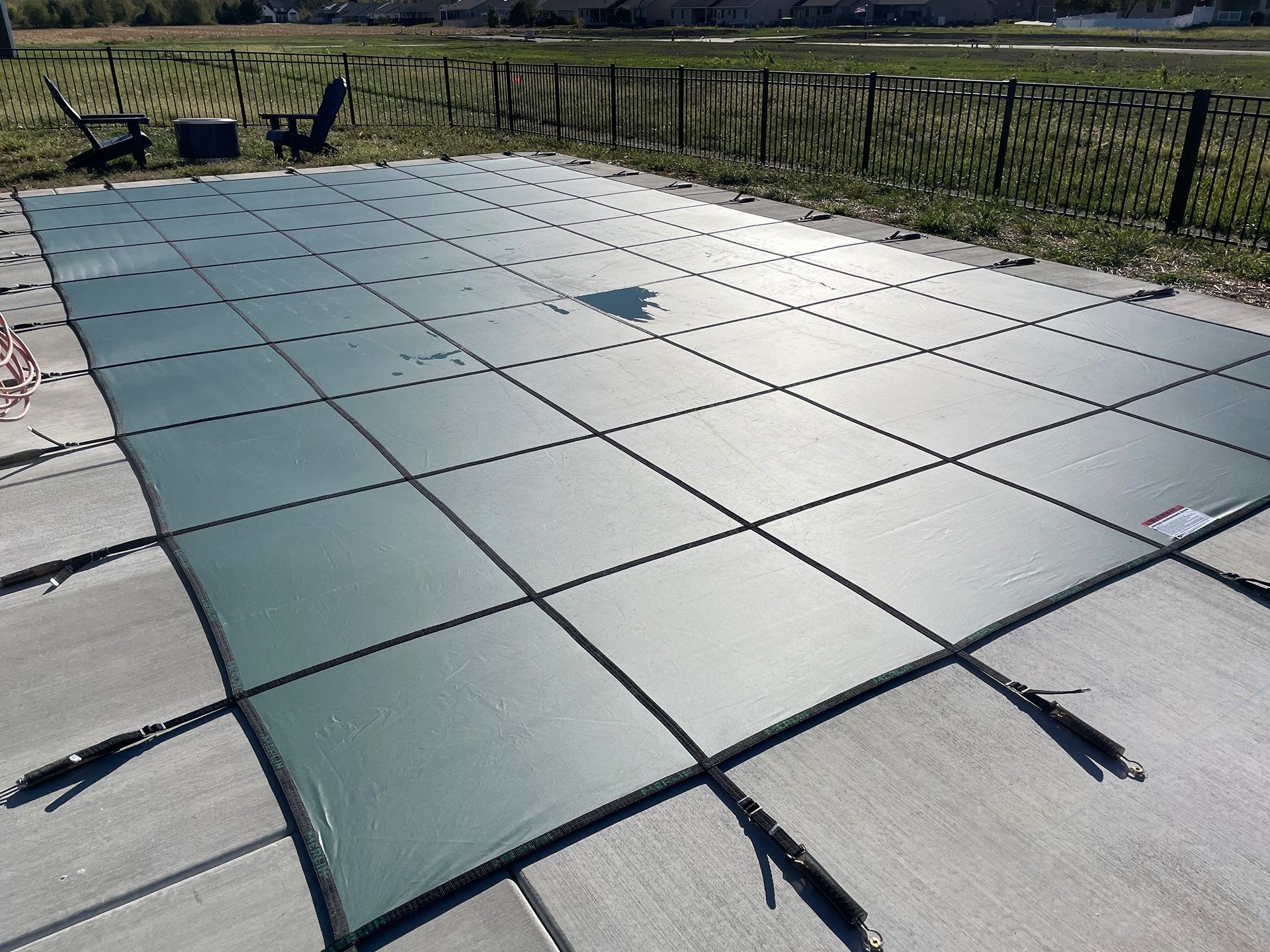 Pool covered with a dark green safety cover on a concrete patio, outdoor setting.
