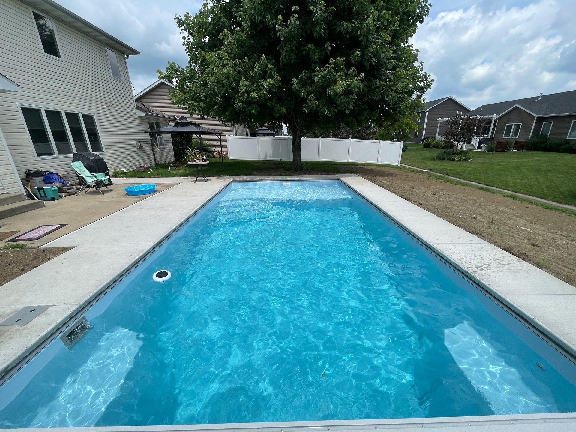 Rectangular blue pool surrounded by a concrete border and grass, in a backyard setting.