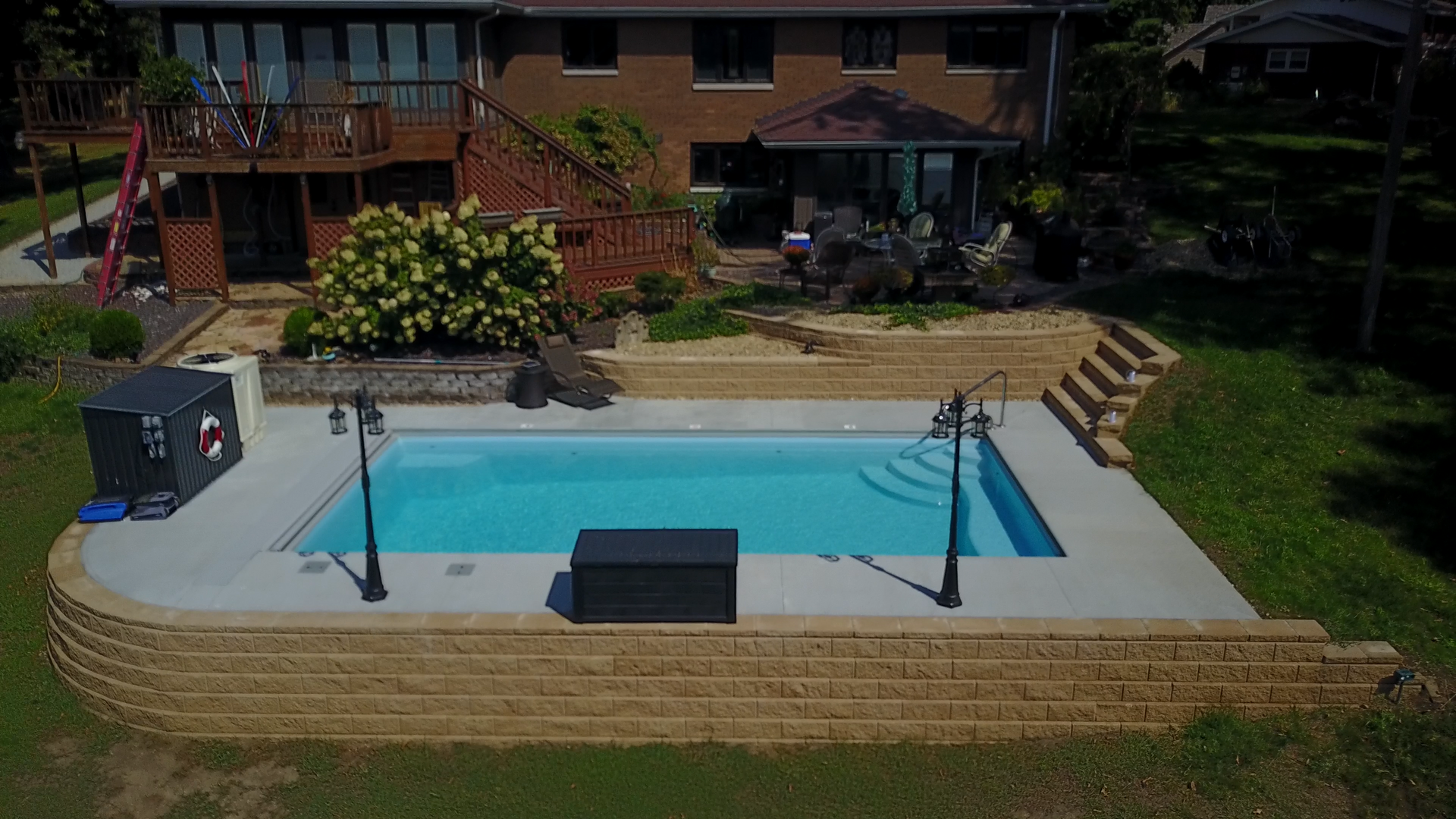 Backyard pool with tan retaining wall, blue water, and house in the background.