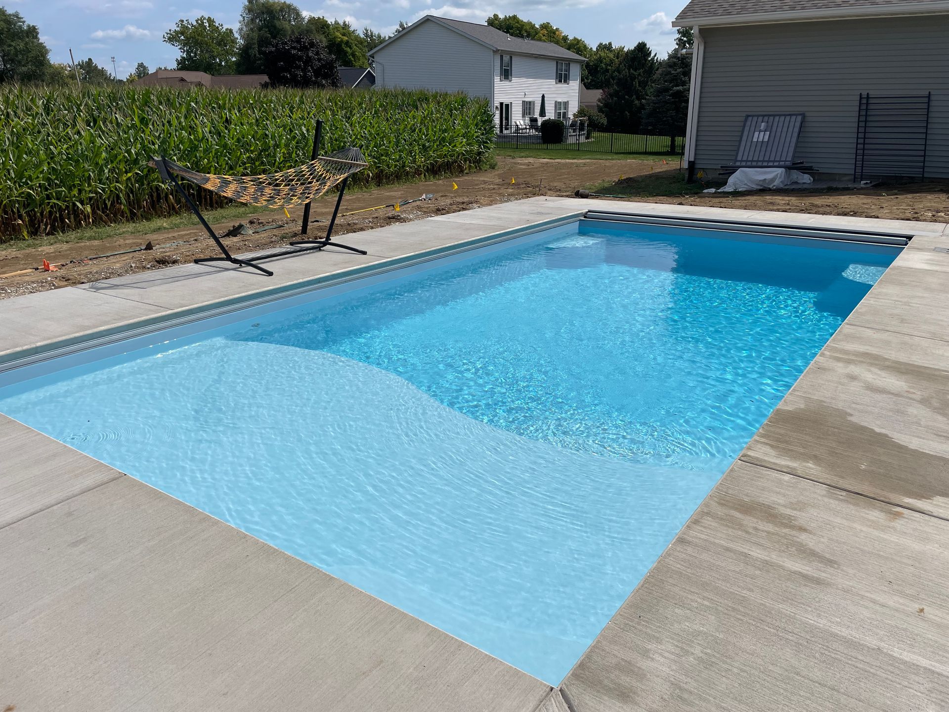 Rectangular pool with clear blue water and concrete surround. A hammock is nearby.