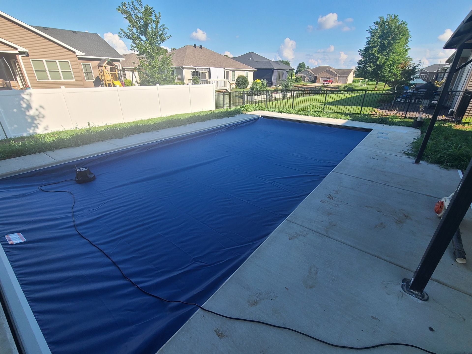 Blue pool cover over a rectangular pool in a backyard with houses in the background.