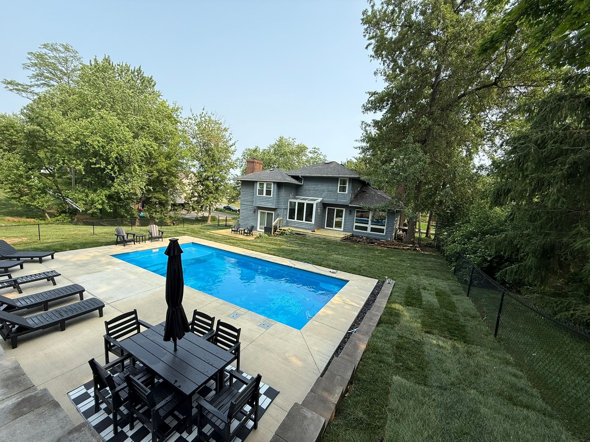 Backyard with a pool, patio furniture, and a two-story gray house.