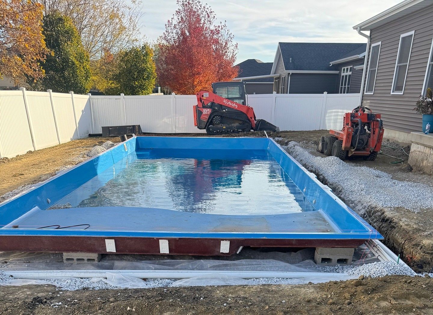 A rectangular blue swimming pool under construction in a yard, with small construction equipment nearby.