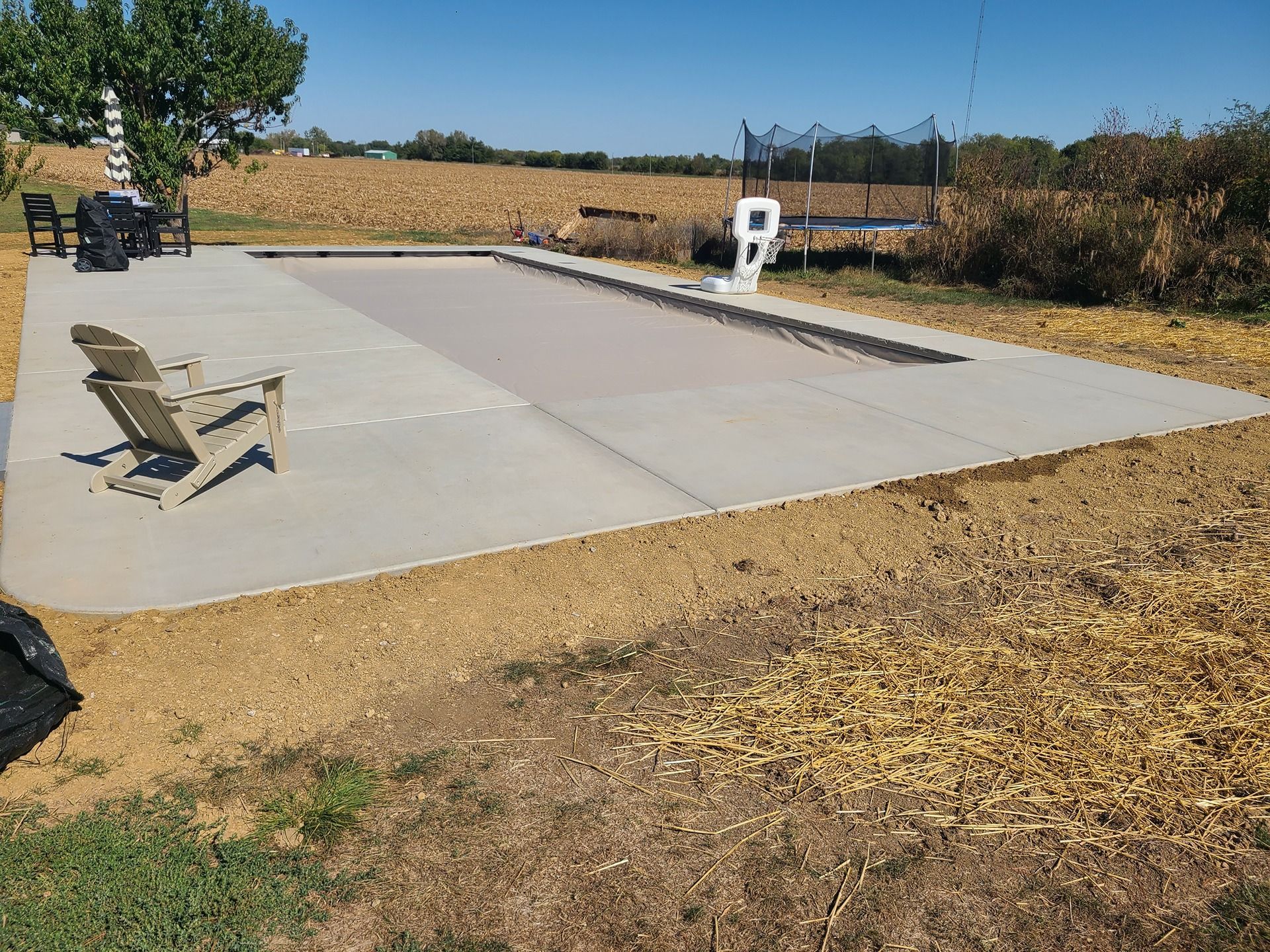 Pool with gray concrete deck and brown pool cover in grassy field.