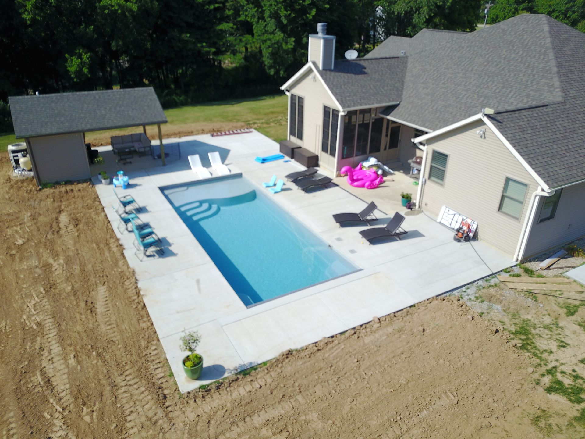 Aerial view of a rectangular pool with patio furniture beside a house and a small shed.