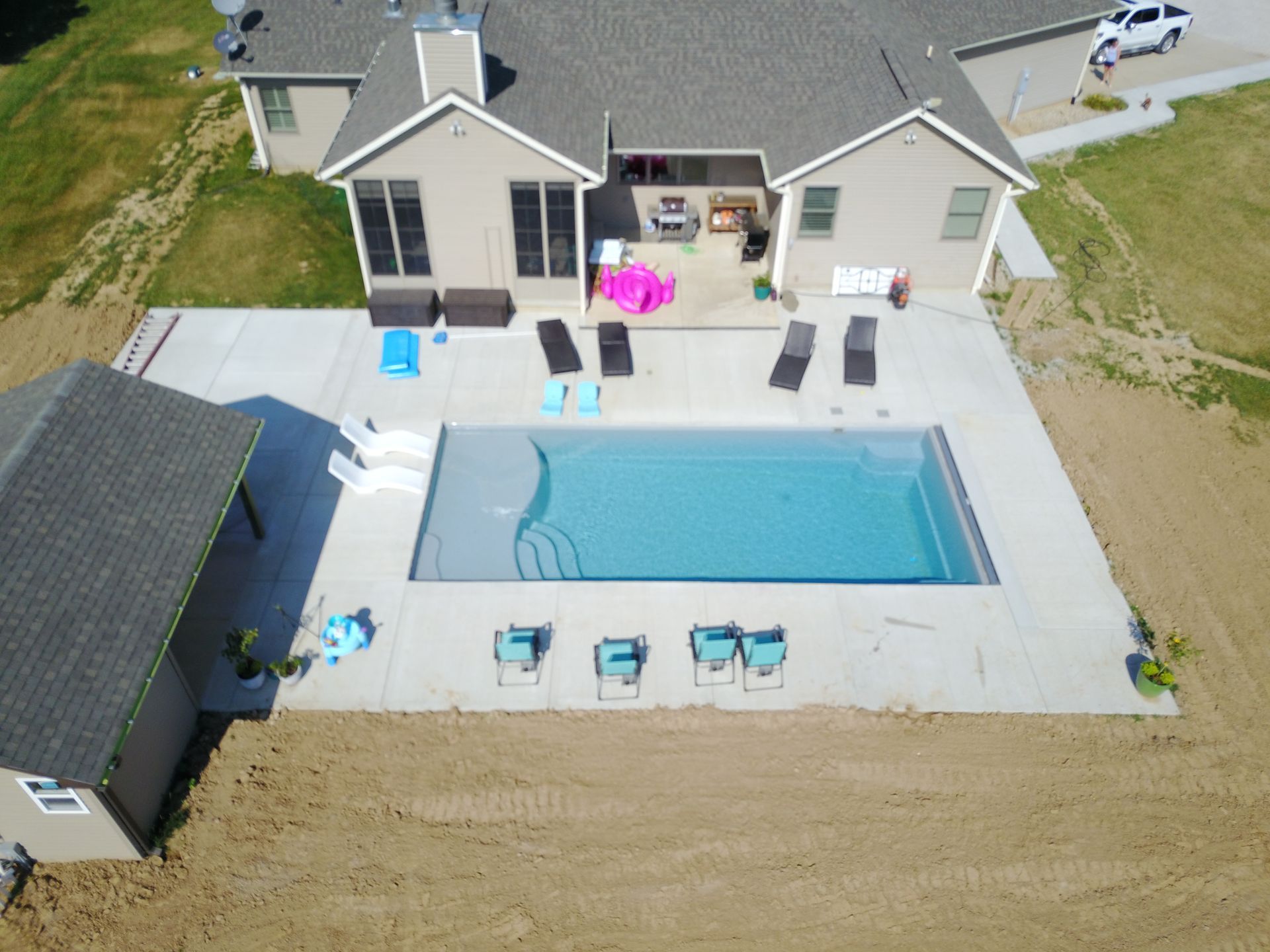 Aerial view of a rectangular pool with surrounding concrete patio and house. Several lounge chairs