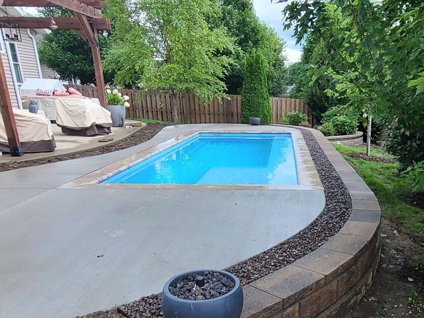 Rectangular backyard pool surrounded by concrete, a retaining wall, and landscaping.
