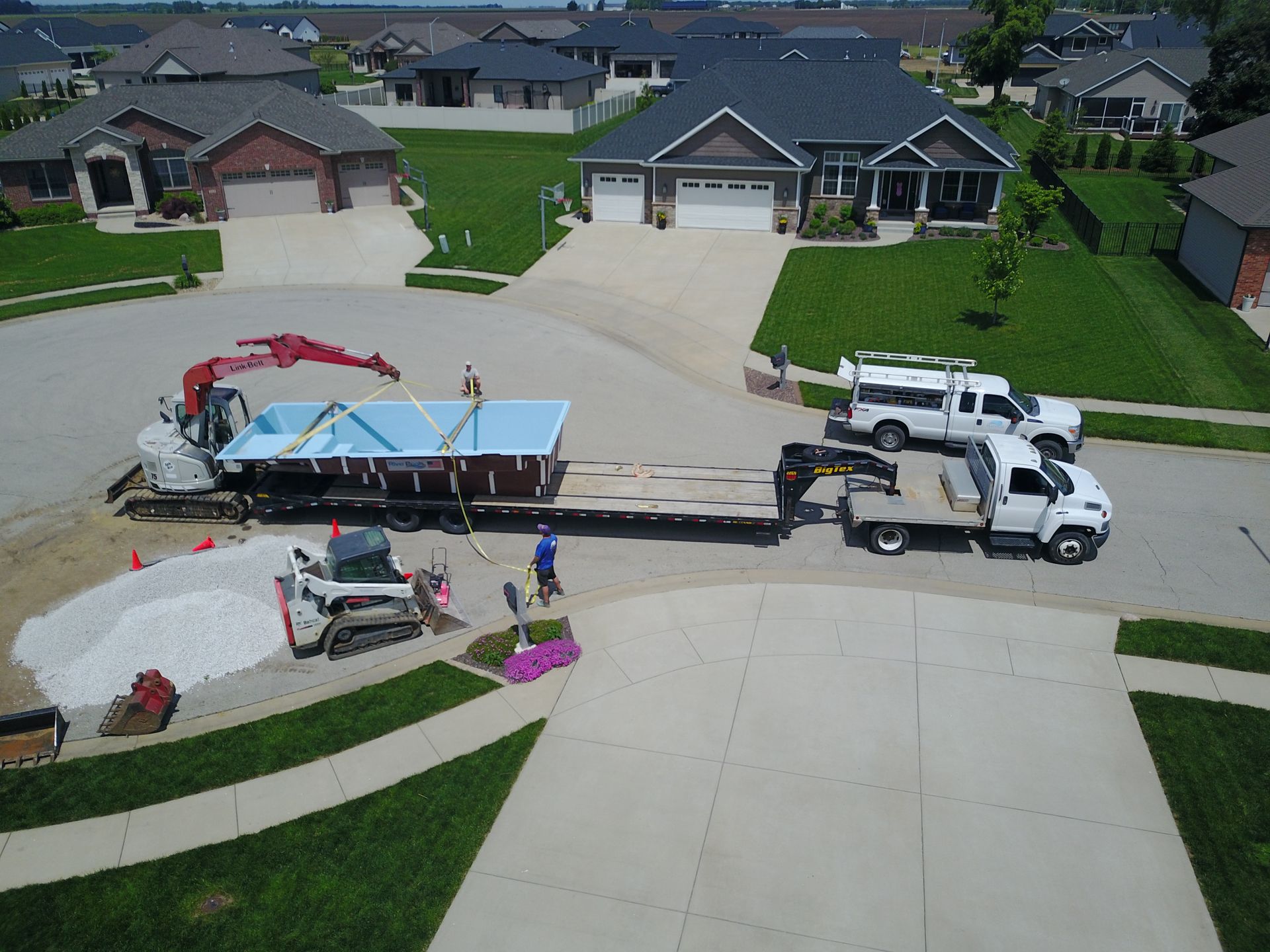 Construction site: Excavator and trucks unloading a pool in a residential neighborhood.