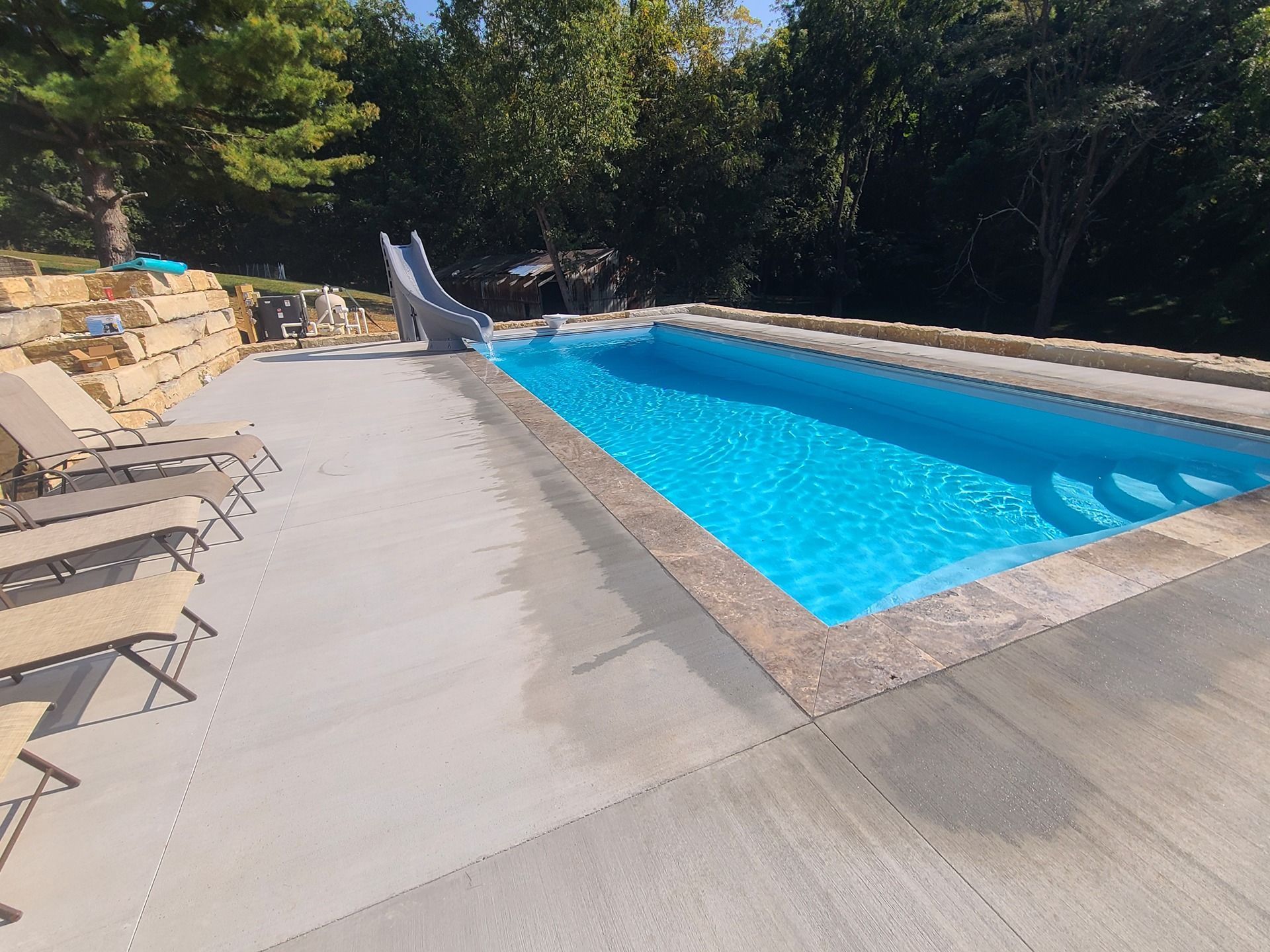 Pool with blue water and stone deck, slide, and lounge chairs.