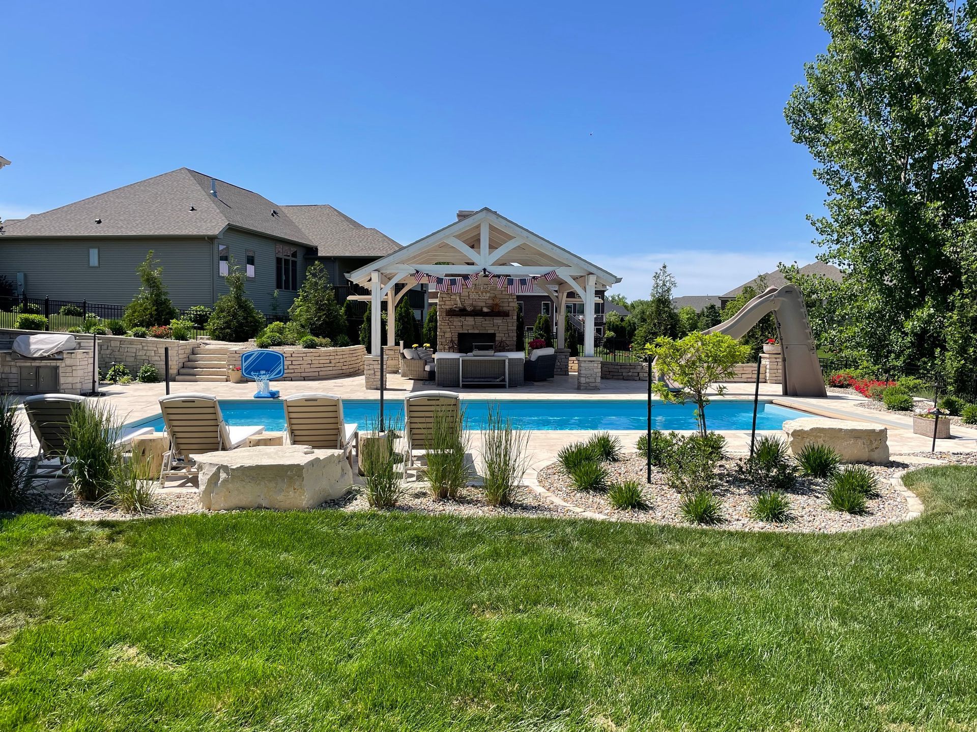 Backyard pool with a covered bar area, lounge chairs, and a slide.