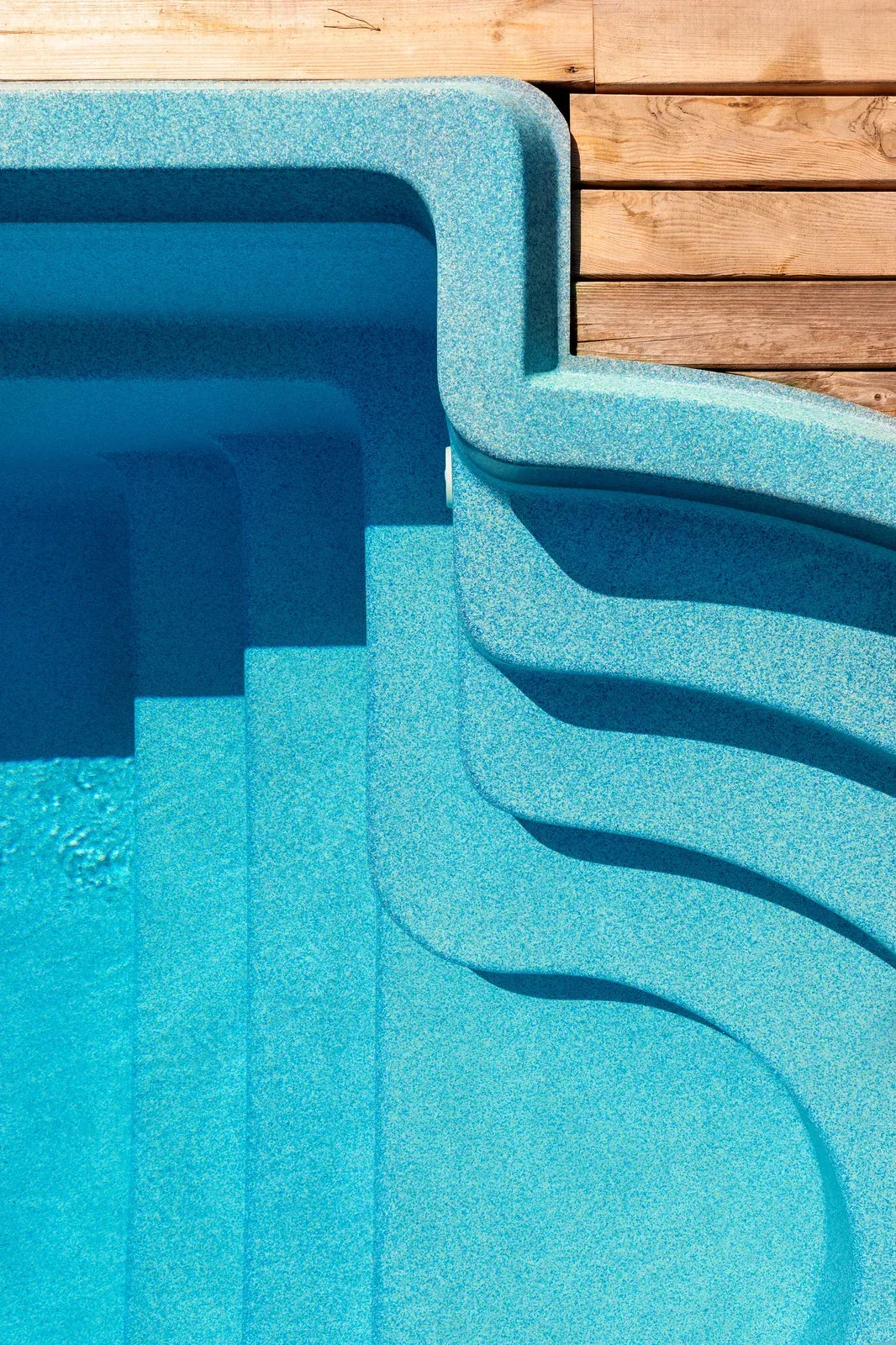 Blue textured swimming pool steps next to wooden deck.