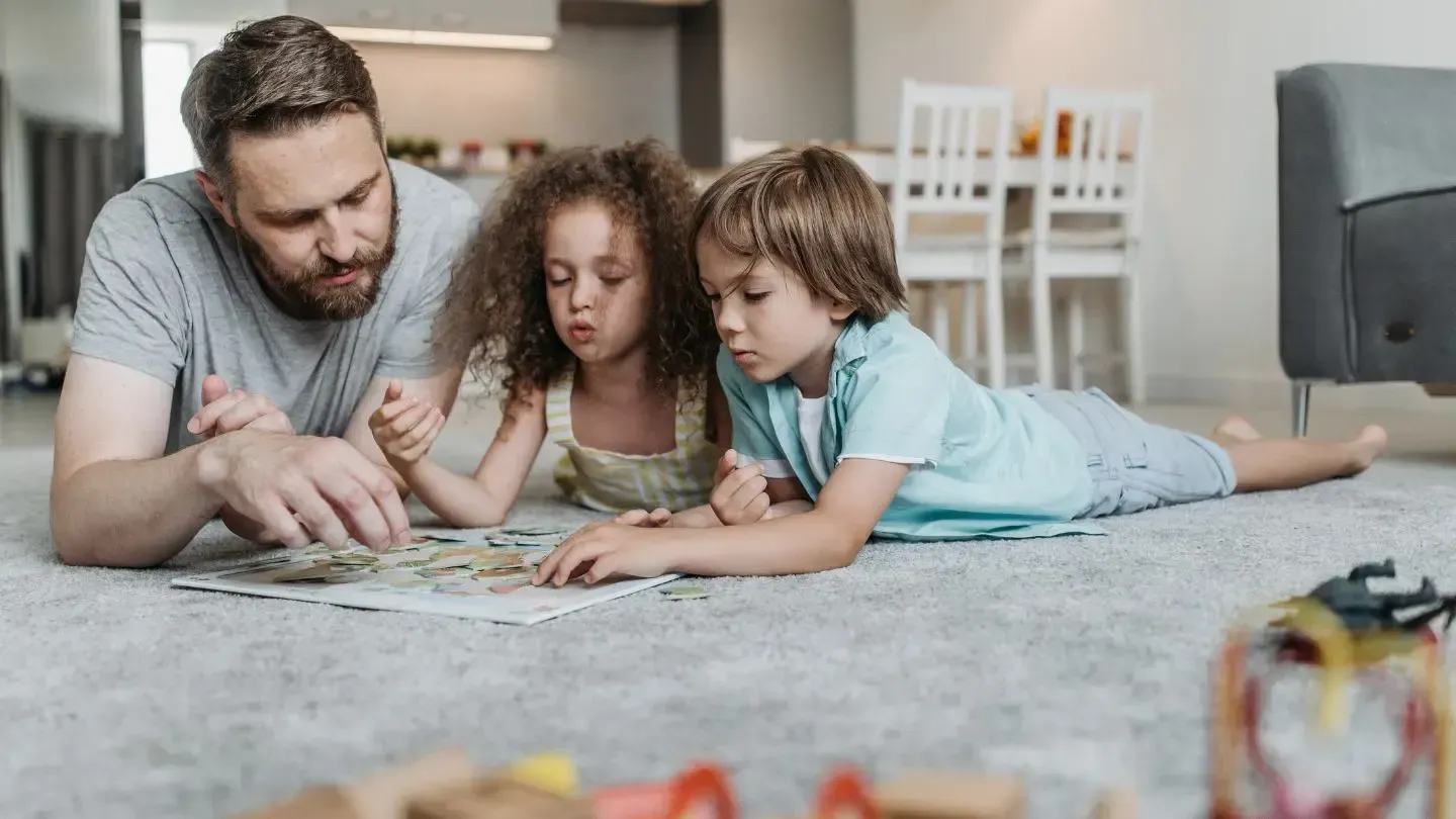 A man and two children are laying on the floor reading a book.