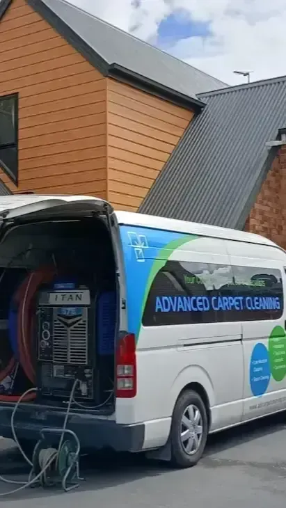 A white van with Advanced Carpet Cleaning equipment parked in front of a house.