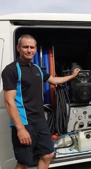 Kerry Walker of Advanced Carpet Cleaning in a blue and black shirt is standing in front of a van.